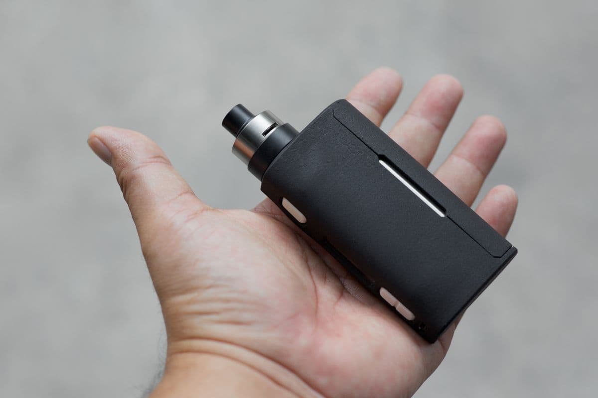 A person holding a black vape mod in his hand
