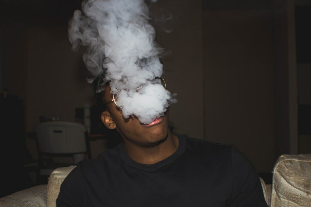 Man wearing black crew neck blowing smoke