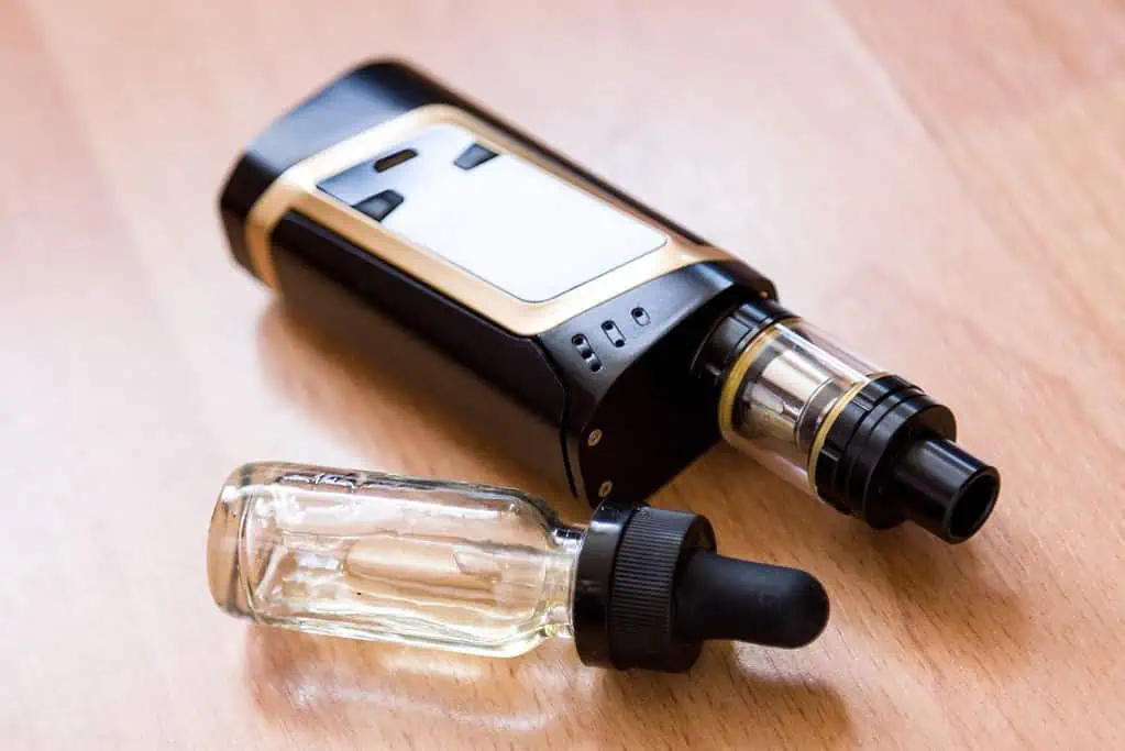 An electronic vaping device and a vape juice glass bottle on a table.