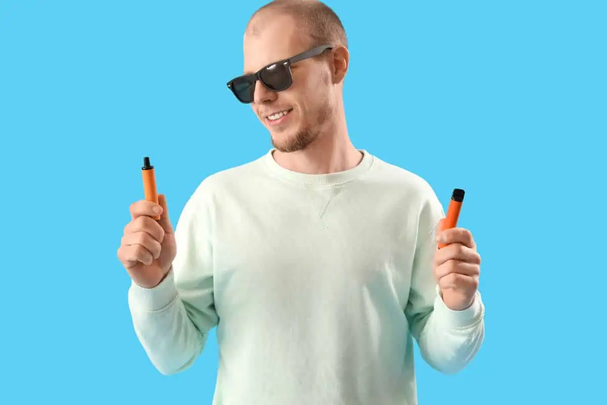 A guy holding two vape devices with different flavors in his hand