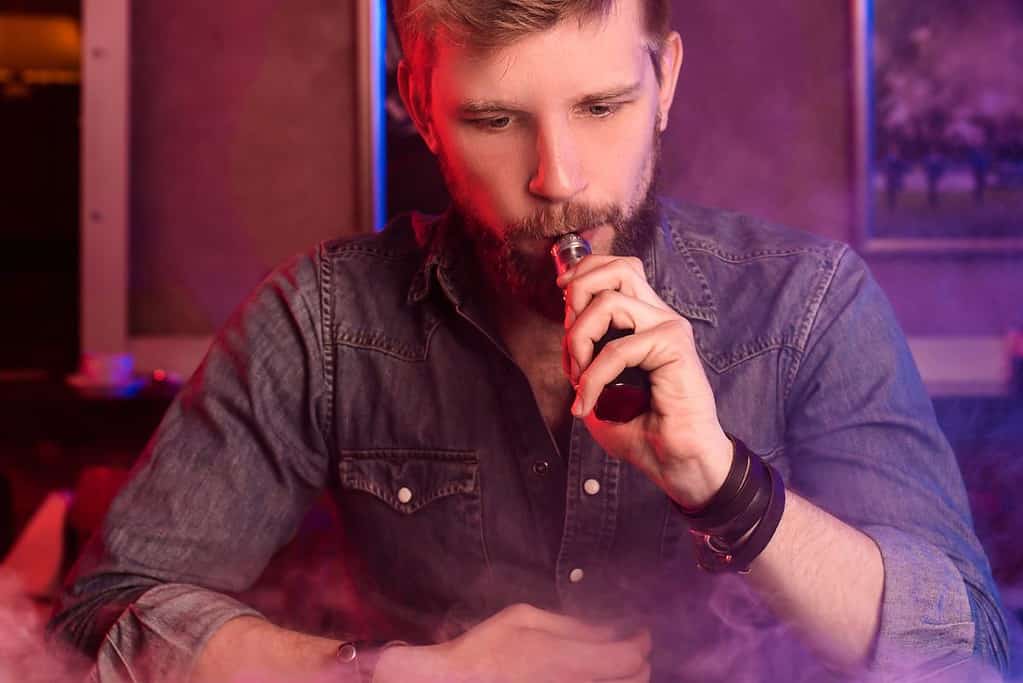 A man vaping in a smoke filled room.