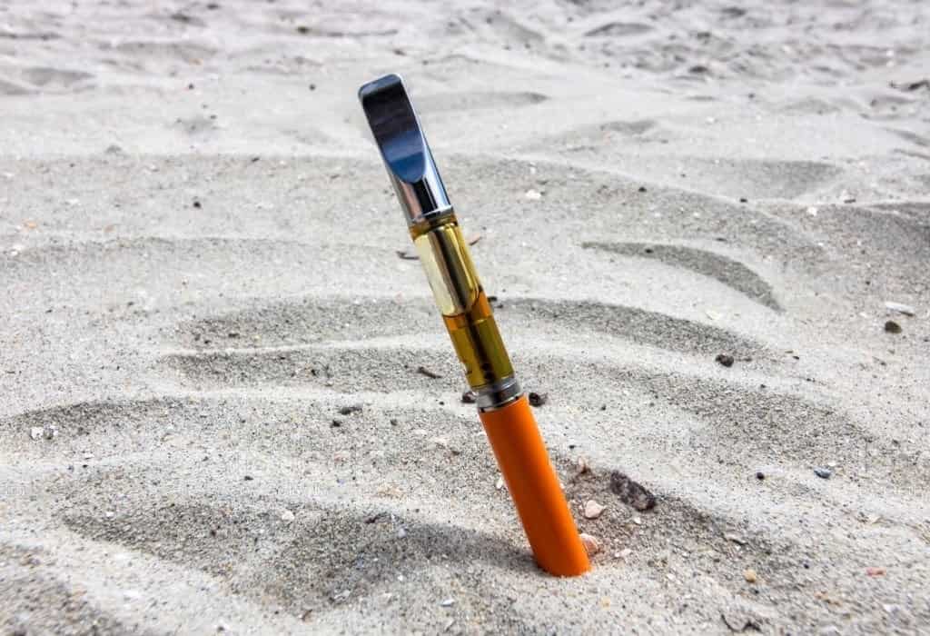 Electric vape pen with orange flavor resting in the sand