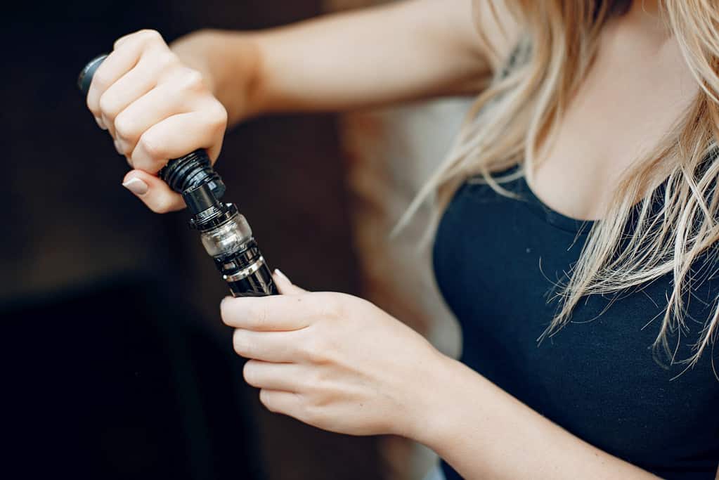 A close up of a lady refilling vape device with eliquid