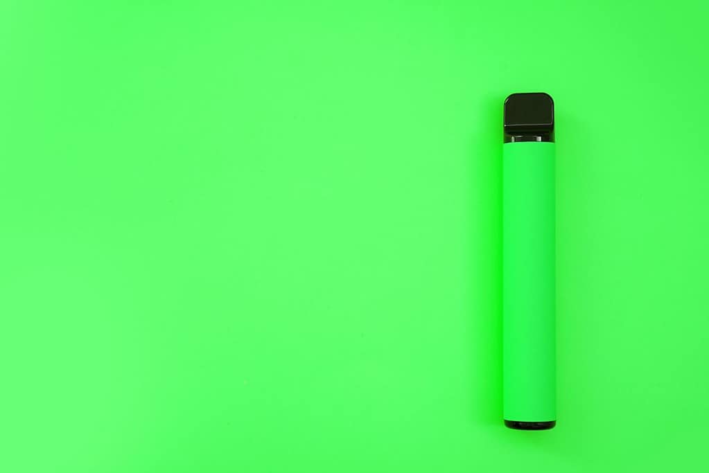 A green disposable vape sitting on top of a green surface.