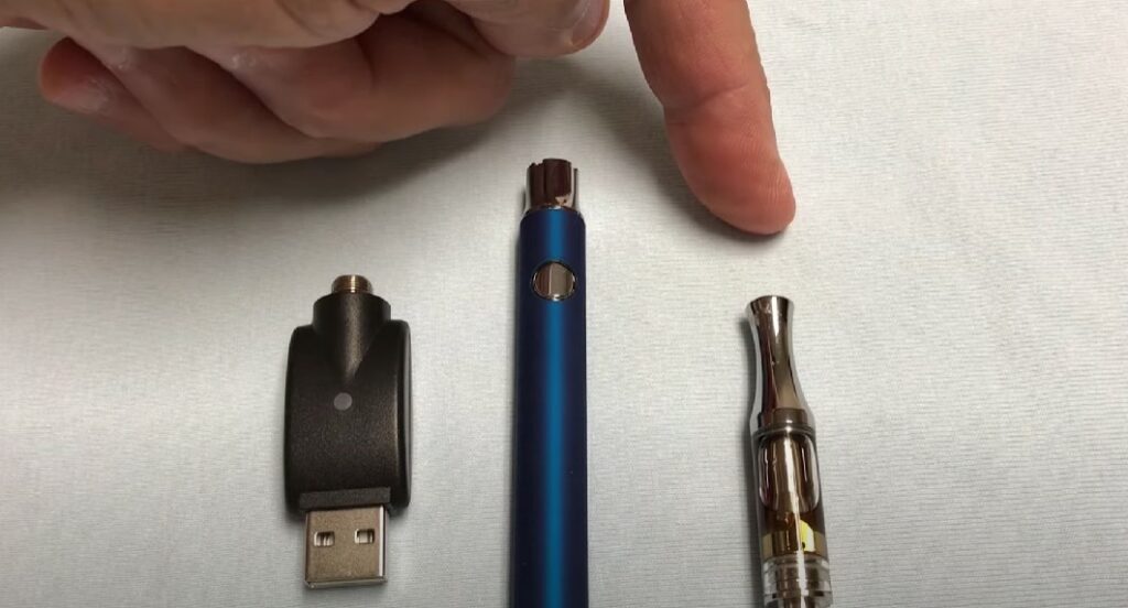 A person is pointing at a vape cart with a vape pen