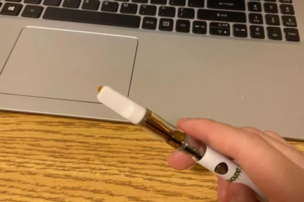 A guy holding a vape pen and wax coming out of its cartridge mouthpiece