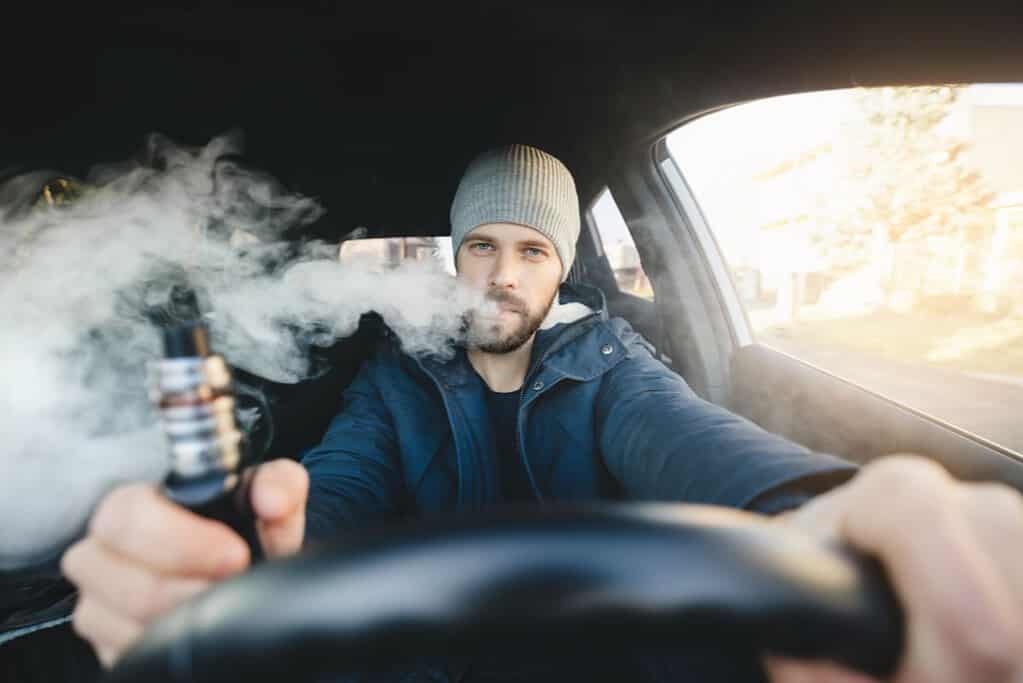 A man smoking an e cigarette in a car.