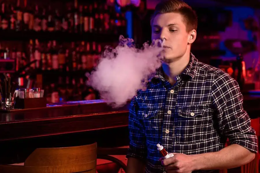 A man vaping an e cigarette in a bar, seeking the cheapest way to vape.
