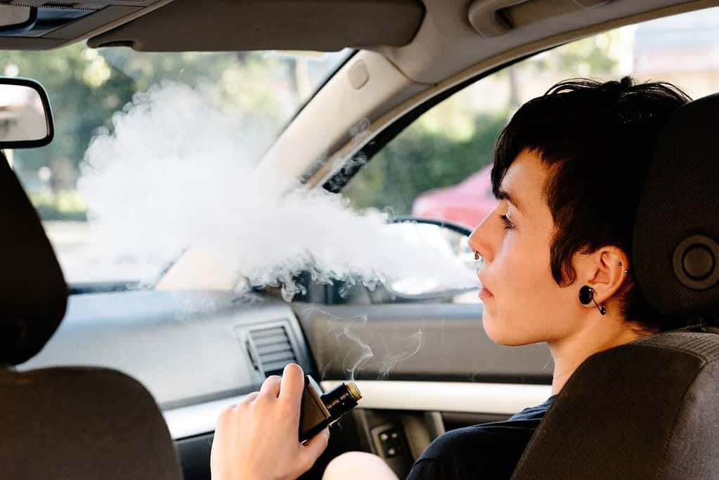 A young woman sitting inside a car and vaping