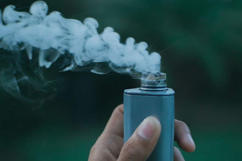 A person demonstrating the meaning of rba vape by holding an electronic cigarette with smoke coming out of it.