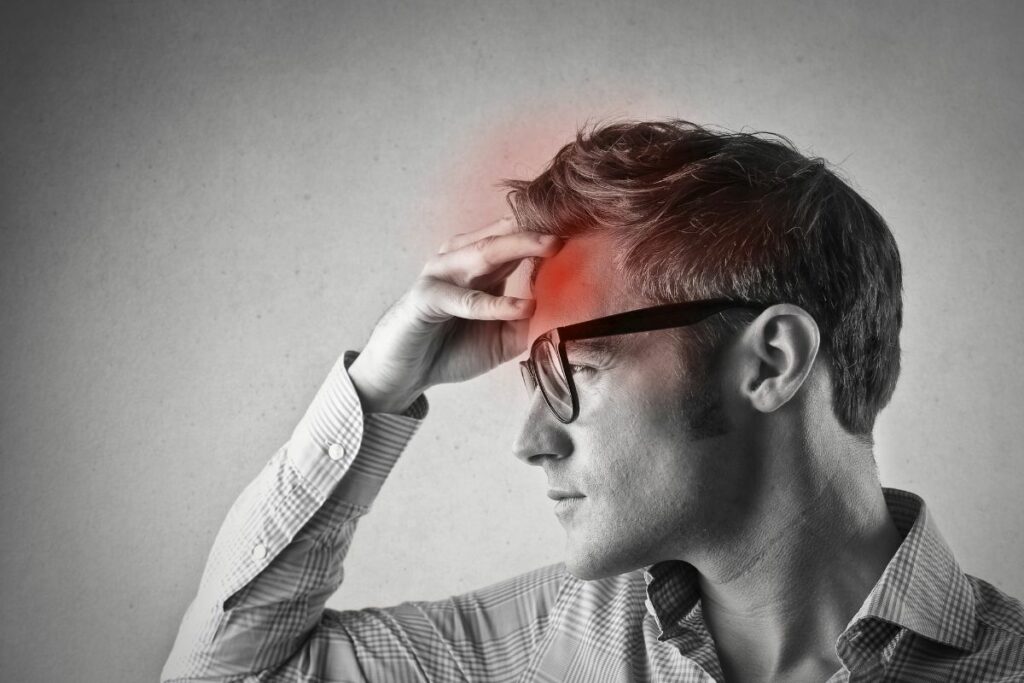 A man in glasses is holding his head in pain
