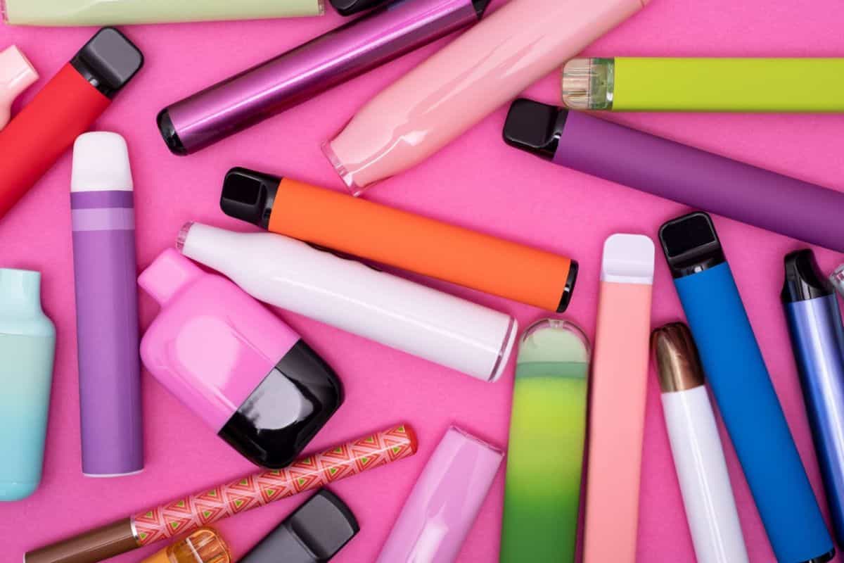 Top 8 Best Vapes Made in the USA: Quality and Innovation 5 A variety of colorful disposable vape pens and e-cigarettes are scattered on a bright pink background, displaying different shapes, sizes, and designs.